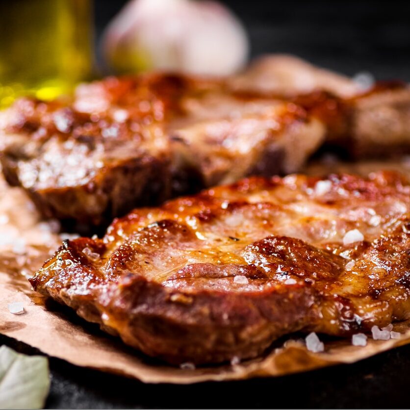 Grilled pork steak on paper on the table. On a black background. High quality photo