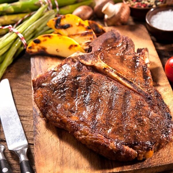 Beef steaks with grilled vegetables and seasoning on wooden background